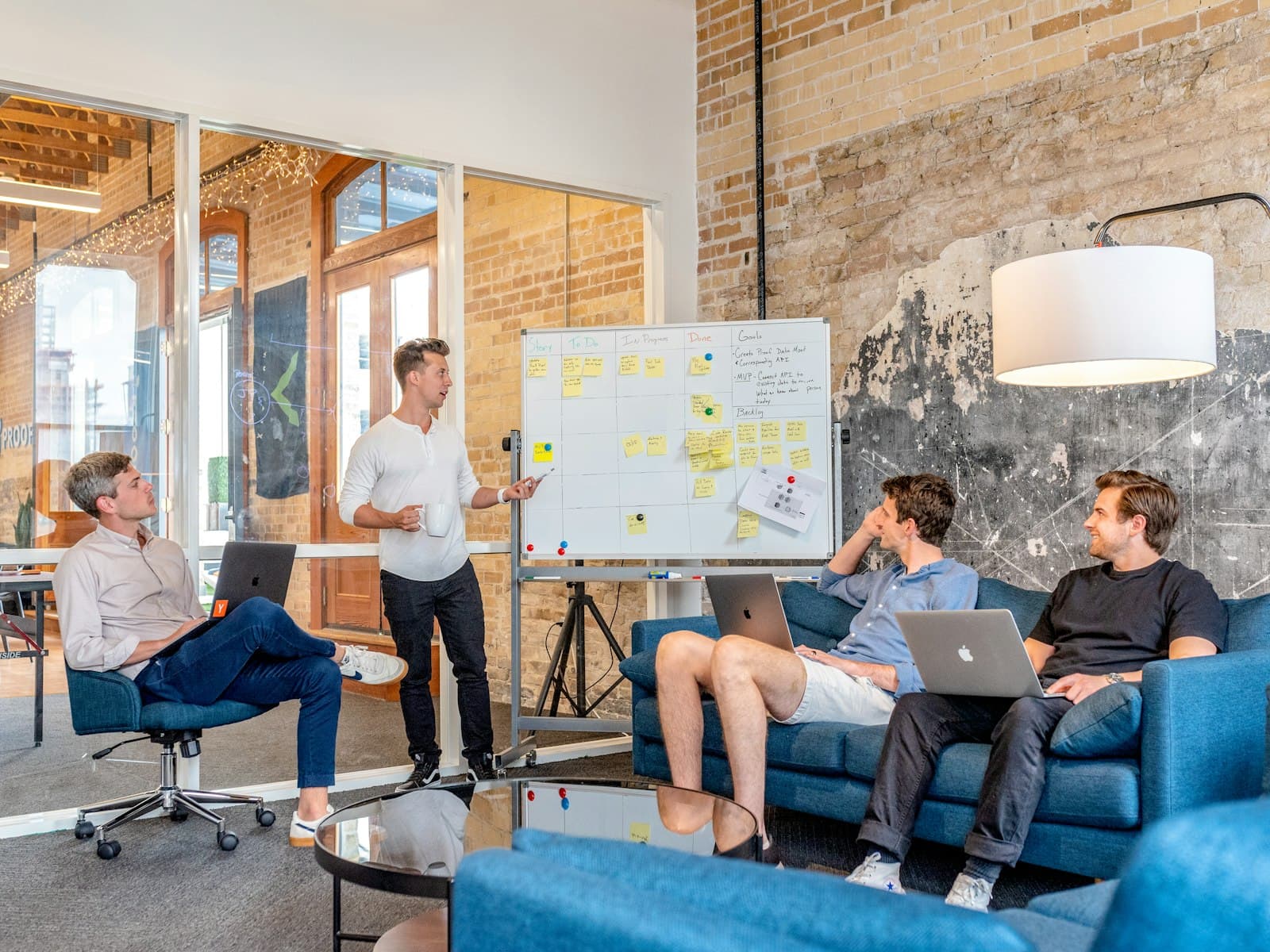 Three people at laptops listening to a colleague at a whiteboard.